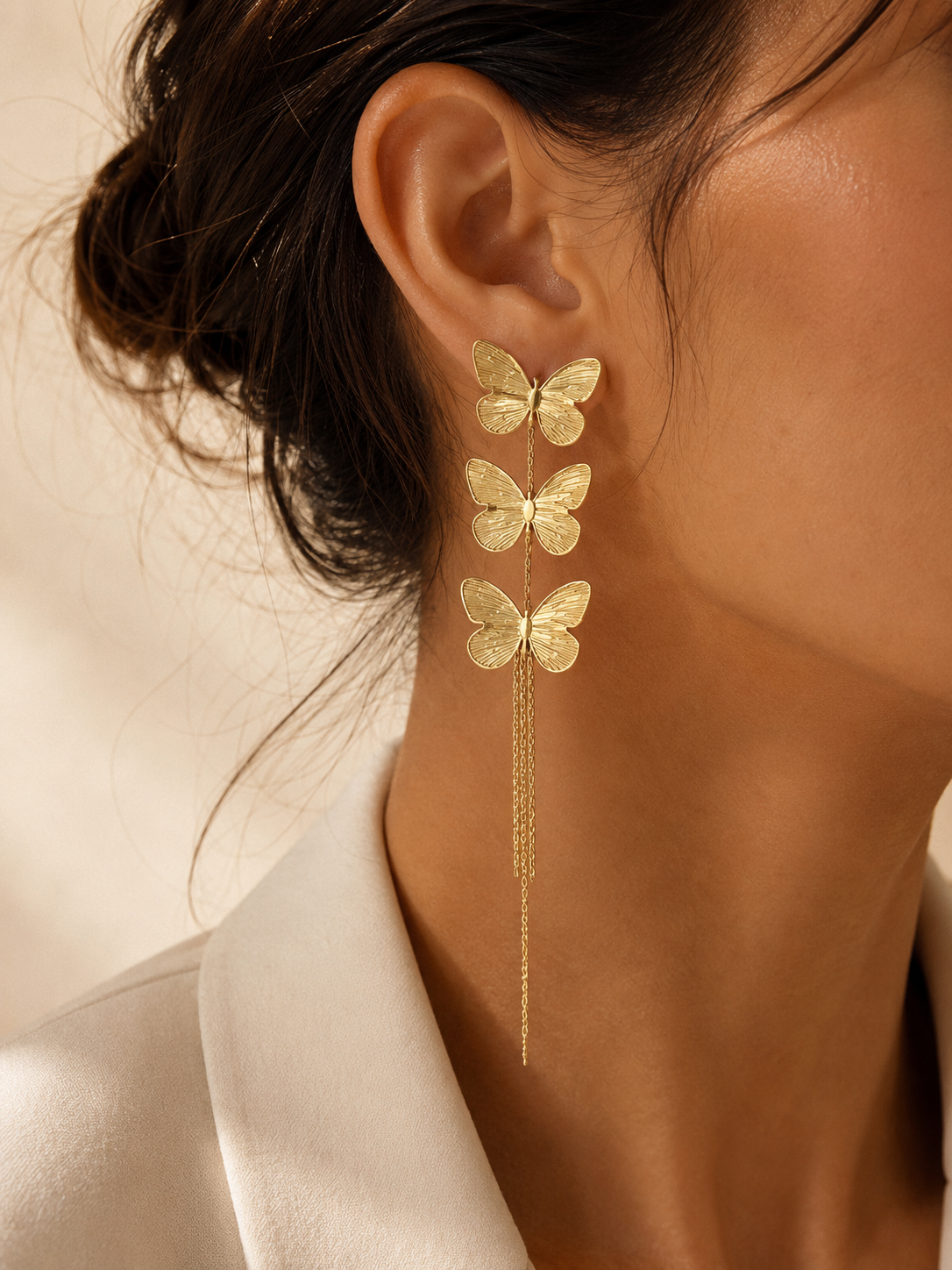 Model wearing The Della Tassel Earrings, featuring cascading gold butterfly charms with delicate tassel chains in steel with 18K gold plating.