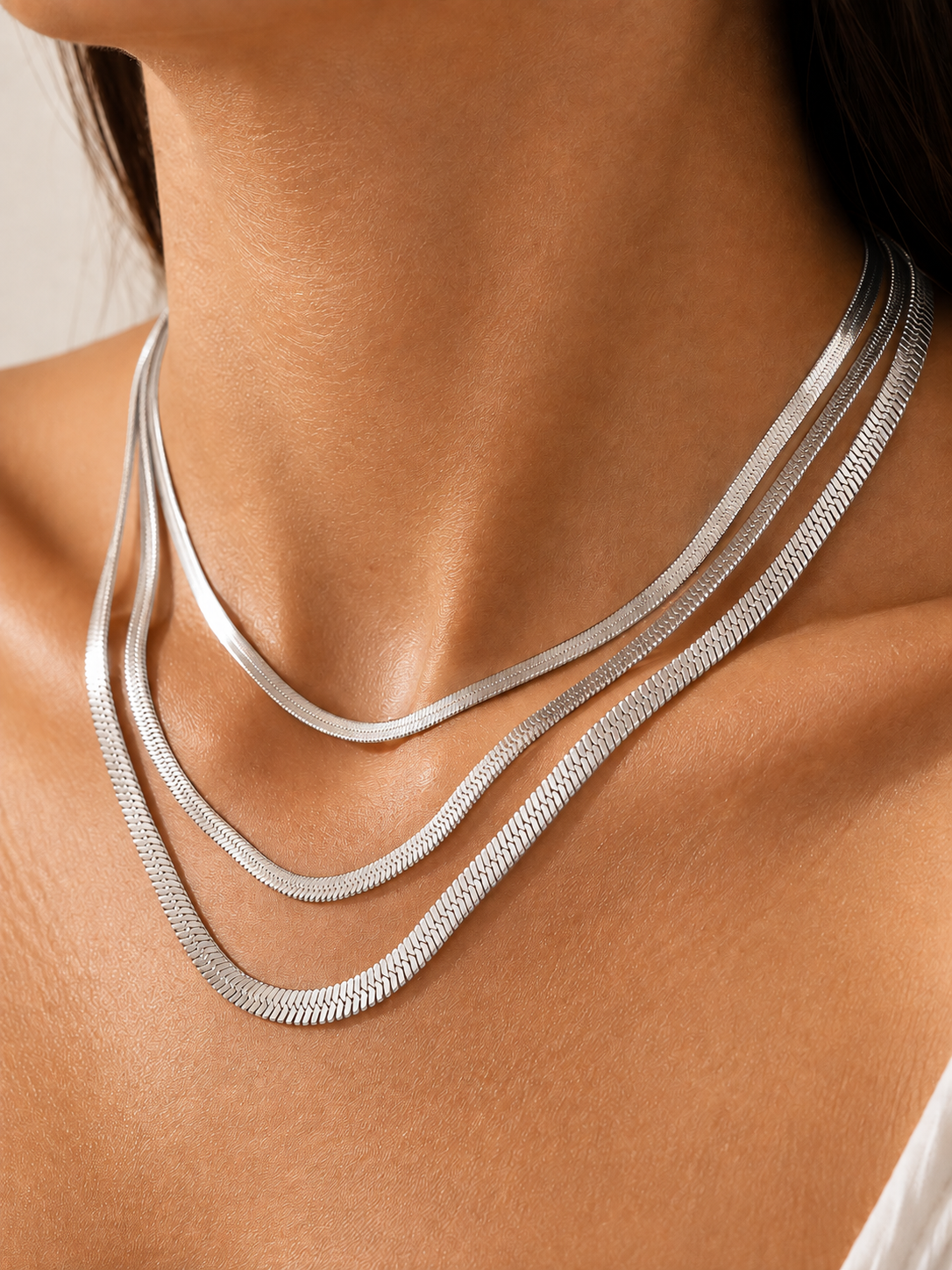Model wearing layered silver snake chain necklaces in 1 mm, 2 mm, and 3 mm widths, crafted from steel.