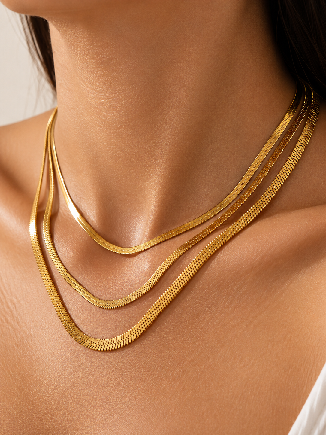 Model wearing layered gold snake chain necklaces in 1 mm, 2 mm, and 3 mm widths, crafted from steel with 18K gold plating.