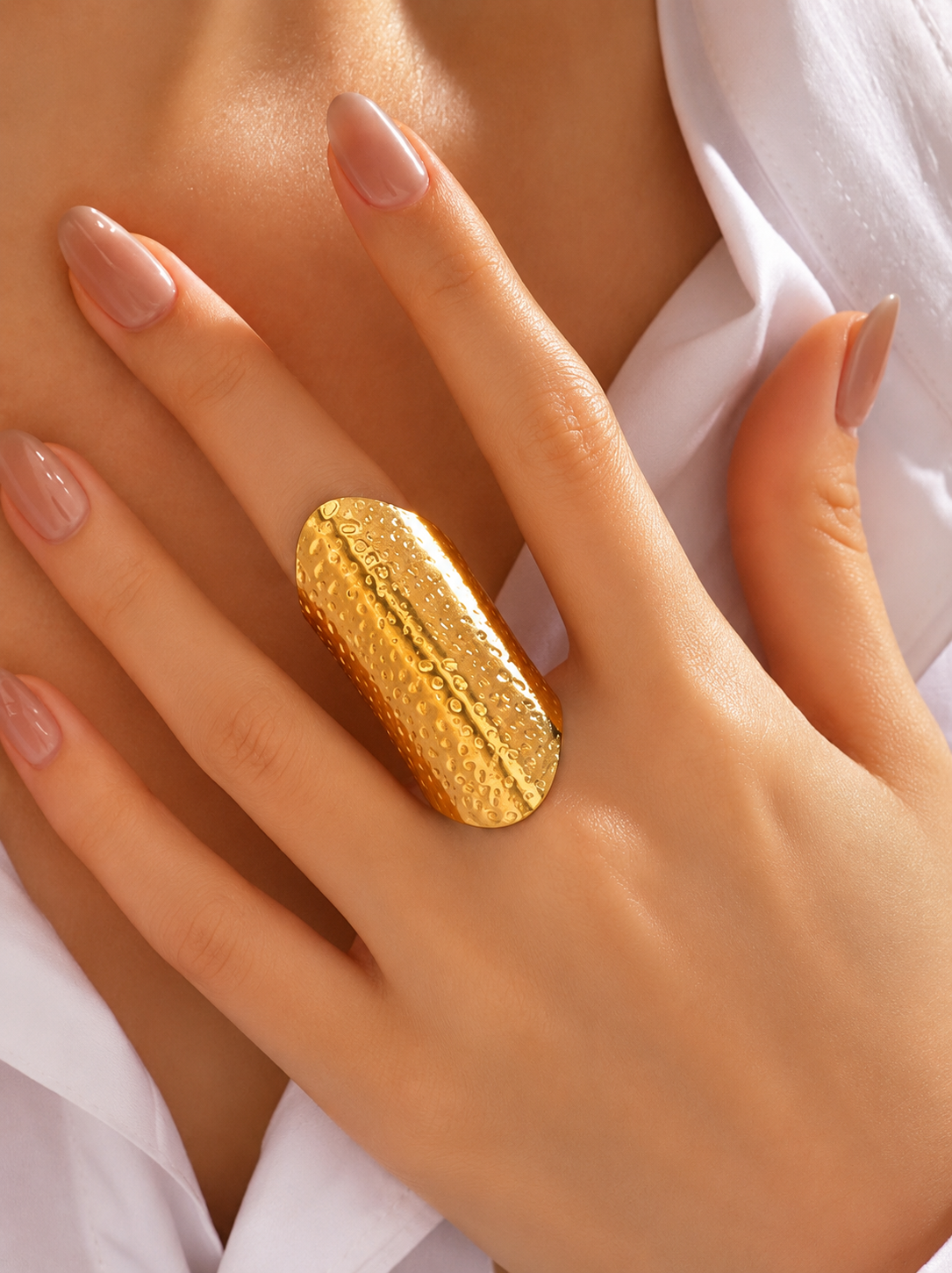 A close-up of a hand wearing a large, textured gold ring with a polished center channel, styled with a white collared shirt.